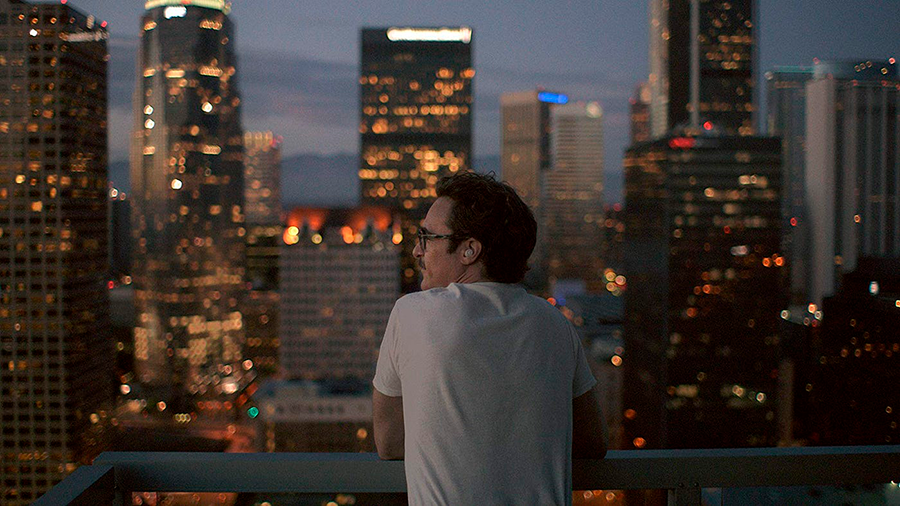 Joaquin Phoenix com uma expressão pensativa e solitária em uma cidade futurística.